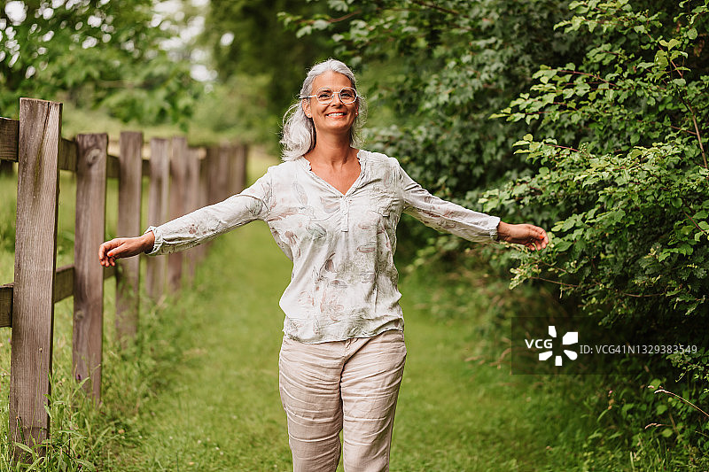 在绿色大自然中张开双臂奔跑的快乐白发中年妇女图片素材