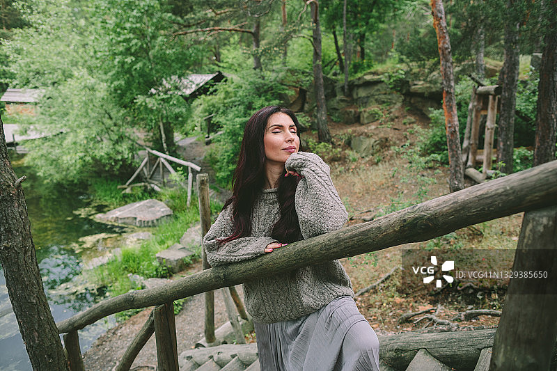 站在森林木梯上的银色长裙棕发年轻女子图片素材