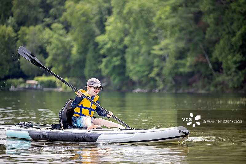 在温暖阳光明媚的夏日度假时，在桨板上划皮划艇的红发小男孩图片素材