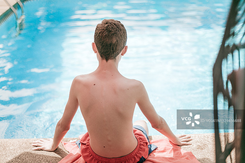 西班牙裔少年坐在游泳池边望向远方的后视图图片素材