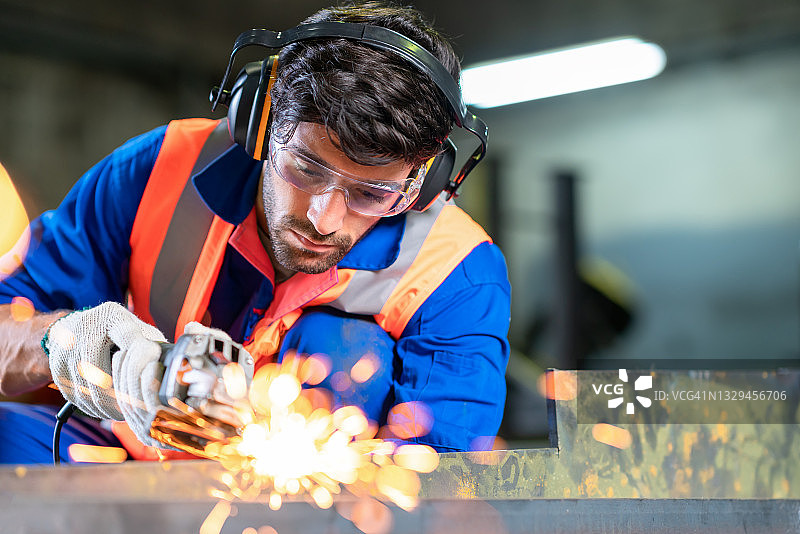 重工业工人用电动砂轮切割钢材。图片素材