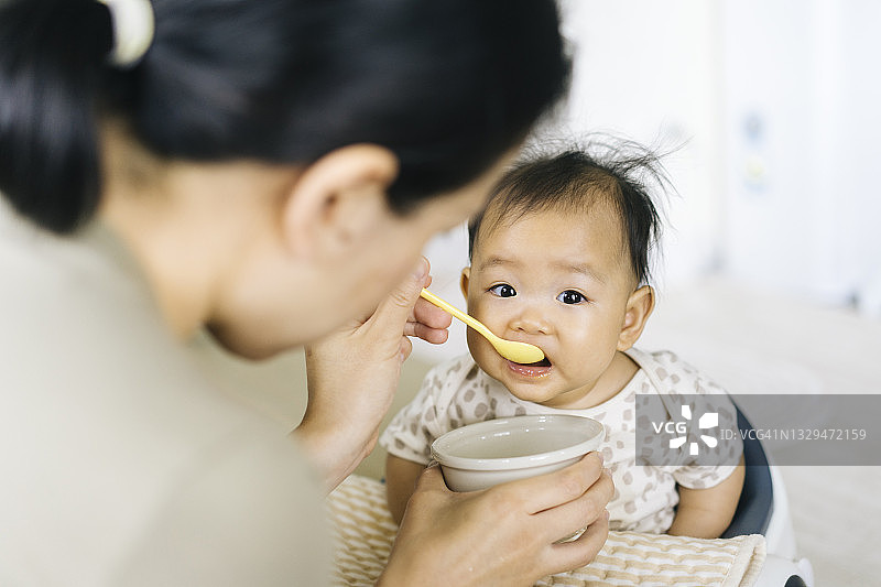 亚洲妈妈尝试喂养和鼓励女儿（2-6个月）在家里的第一餐图片素材