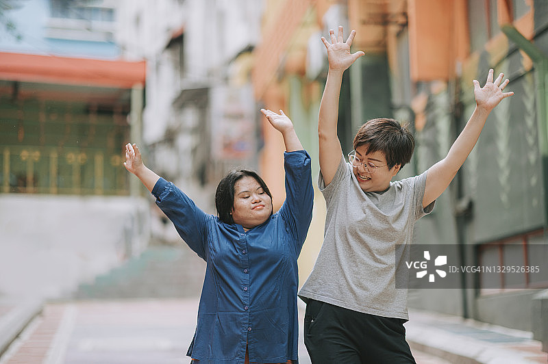 快乐的亚洲马来自闭症唐氏综合征女孩在城市街道上与她的女性朋友一起跳舞图片素材