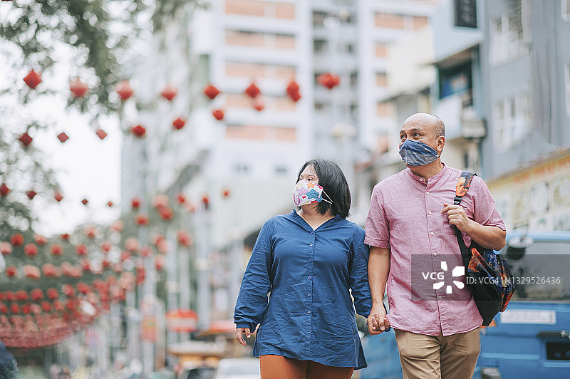 马来西亚退休父亲和他患有唐氏综合征的女儿在周末休闲活动期间戴着口罩牵手走过城市街道图片素材