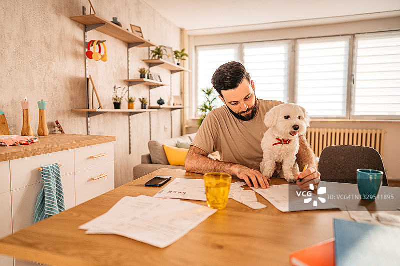 男人在家查看财务状况，狗在腿上图片素材