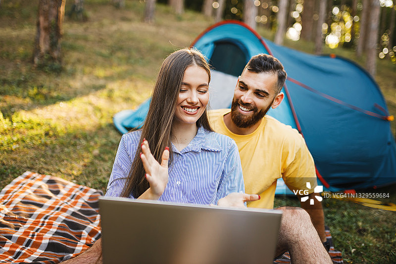 幸福的年轻夫妇在森林里露营时使用笔记本电脑图片素材