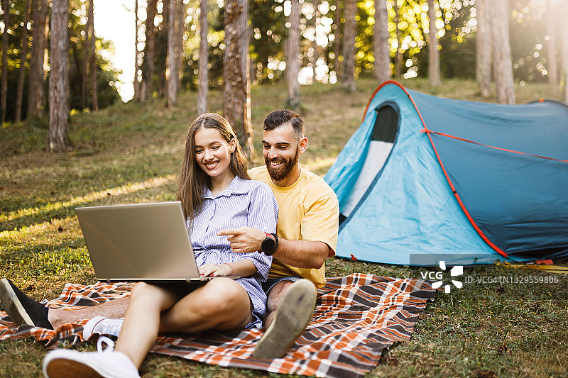 幸福的年轻夫妇在森林里露营时使用笔记本电脑图片素材