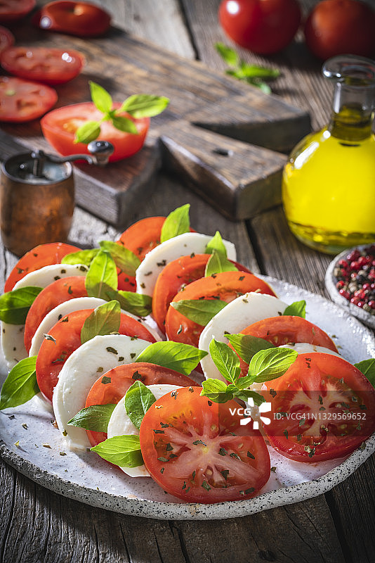 卡普雷塞沙拉：番茄、马苏里拉奶酪、牛至和橄榄油，乡村木桌图片素材
