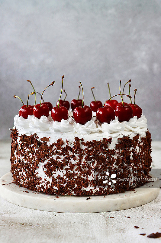 蛋糕架上的黑森林蛋糕照片，裱花奶油花饰，顶部放有黑樱桃，豪华巧克力蛋糕，磨砂奶油和巧克力刨花，大理石效果背景，焦点在前图片素材