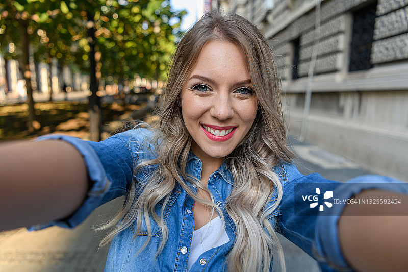 走在城市街道上，用智能手机自拍的年轻女人图片素材