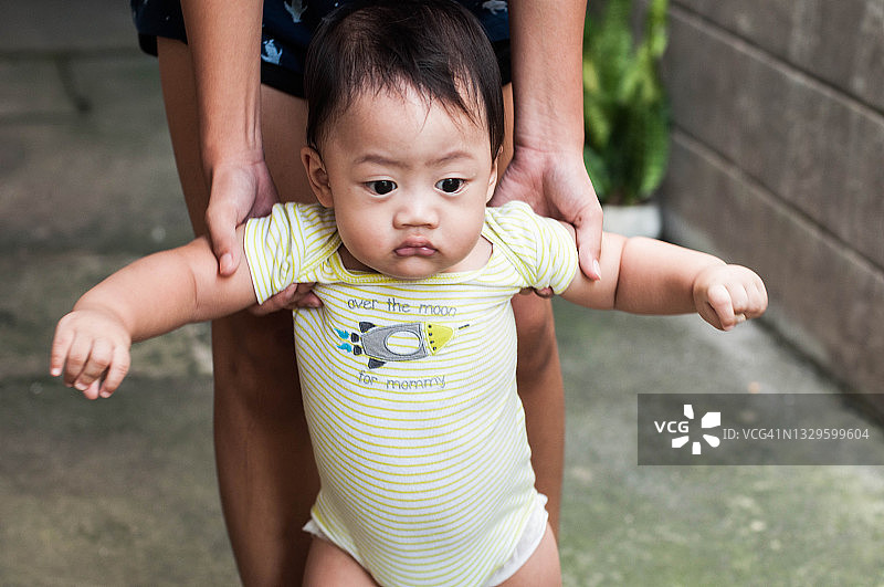 东南亚宝宝在母亲的帮助下在后院学习走路图片素材