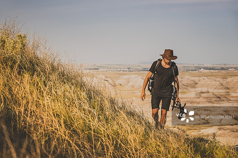 男子在荒地山坡上行走，手持相机图片素材