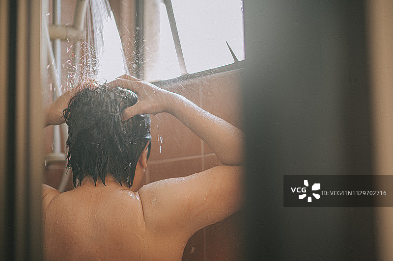 清晨，背光下，中国亚洲女性在浴室用流水洗头图片素材