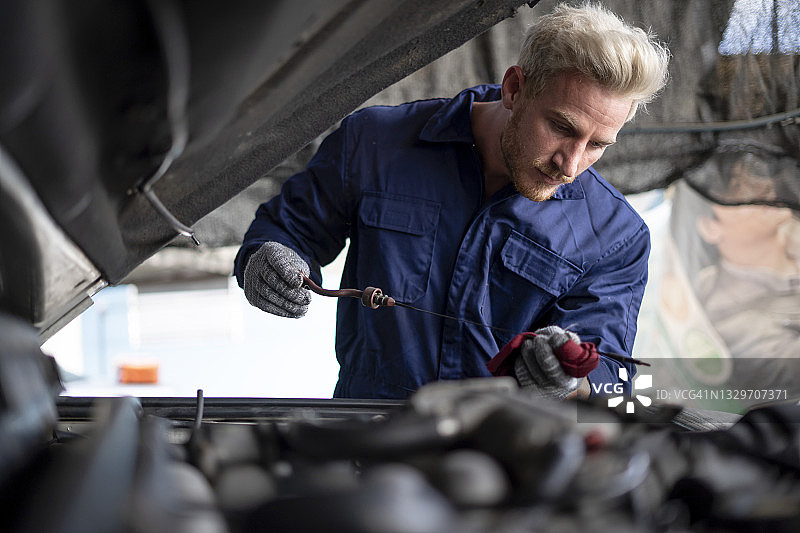 机械专家在汽车修理店用橙色工具检查汽车发动机油位。汽车维护、安全，发动机盖已打开图片素材