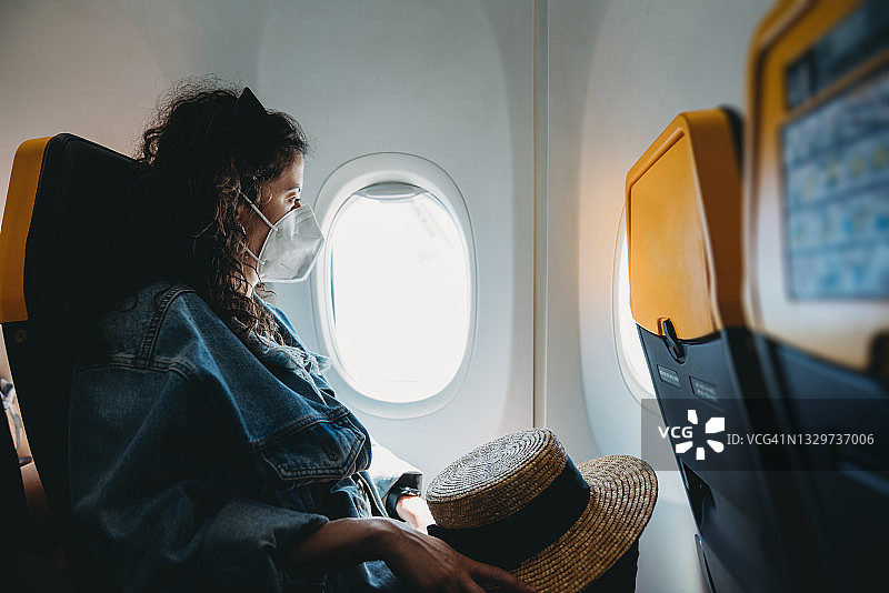 戴防护口罩的女人在飞机上向窗外看图片素材
