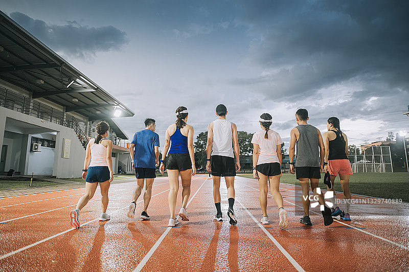 暴风云湿漉漉的地面上，在傍晚训练后走在田径运动场上的亚洲华人运动队背影图片素材