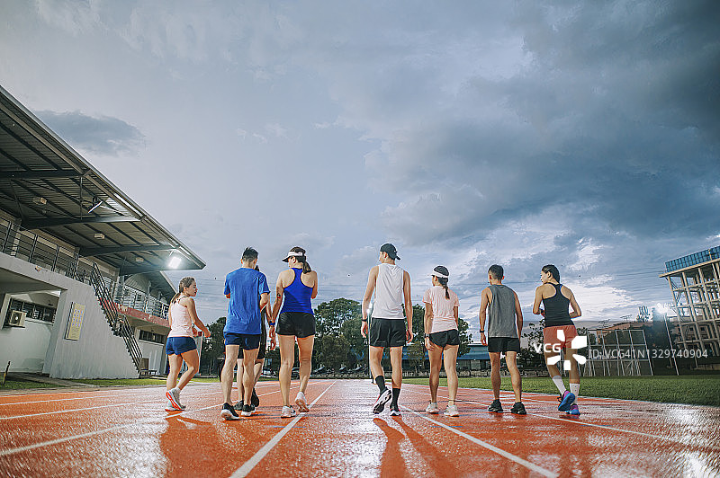 暴风云湿漉漉的地面上，在傍晚训练后走在田径运动场上的亚洲华人运动队背影图片素材