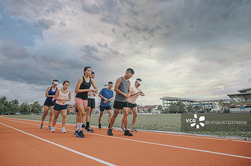 亚洲中国运动员一字排开，准备在田径场上使用智能手表计时跑步图片素材