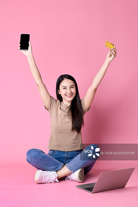 站在粉红色背景下手持手机和信用卡的快乐女商人肖像图片素材