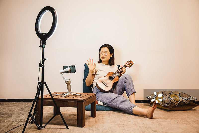 亚洲女性网红用手机在三脚架上拍摄尤克里里vlog图片素材