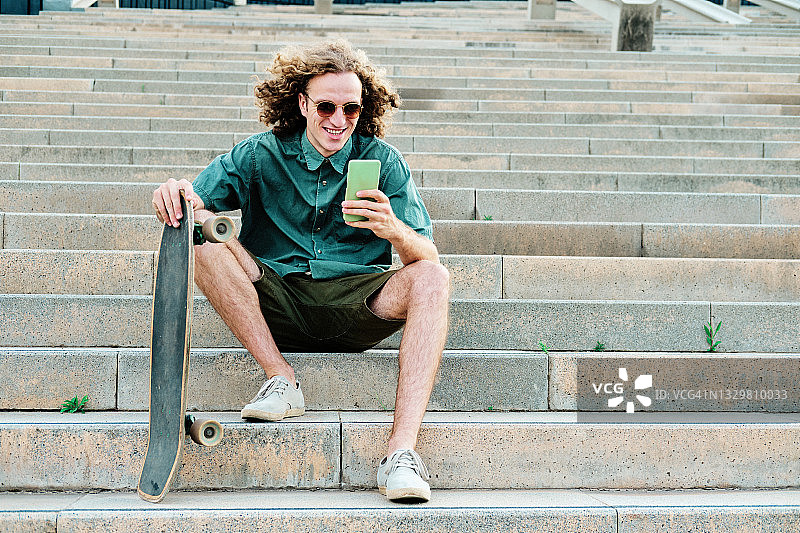 年轻男人坐着玩滑板和智能手机图片素材