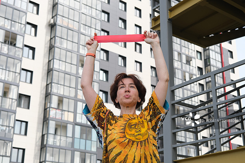 中年妇女在社区用硅胶阻力带锻炼图片素材