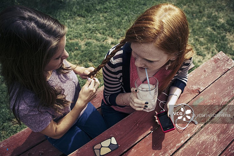 户外，少女为朋友编头发的高角度视图图片素材
