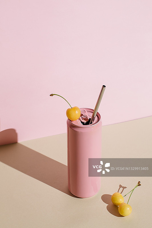 粉色铝制饮料罐配可重复使用的不锈钢吸管和黄色樱桃浆果，粉米色背景。极简艺术静物。零浪费，无塑料概念。图片素材