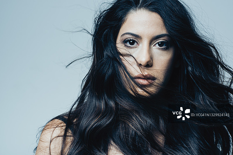 蓝色背景下拥有黑色长发的漂亮年轻女人肖像图片素材