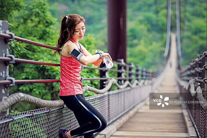 在绳桥上查看智能手表的年轻日本女人图片素材