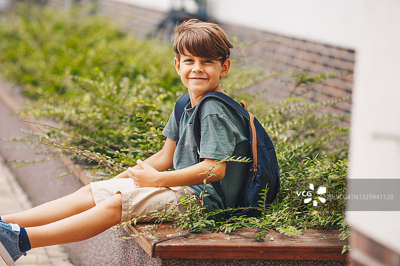 微笑的年轻男孩坐在学校前面图片素材