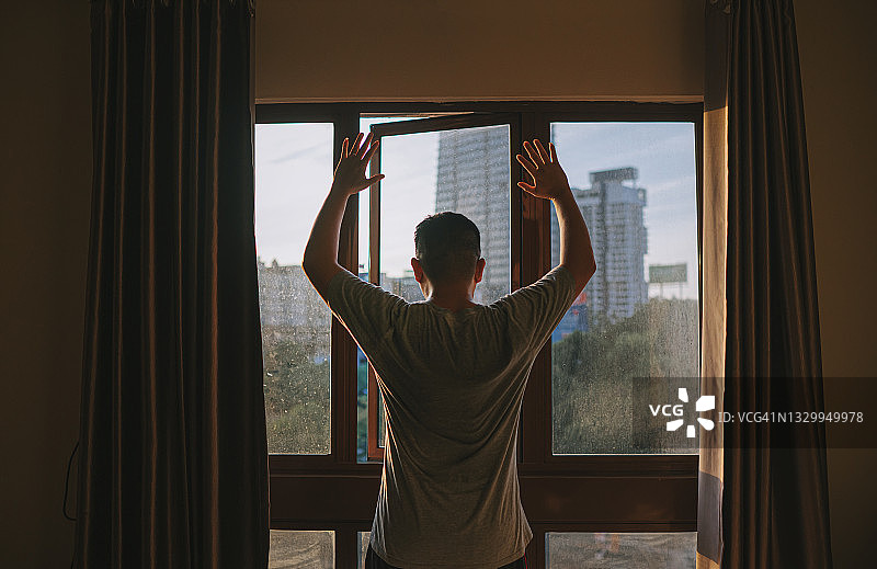 亚裔中年男子在卧室窗前跳跃锻炼的后视图图片素材