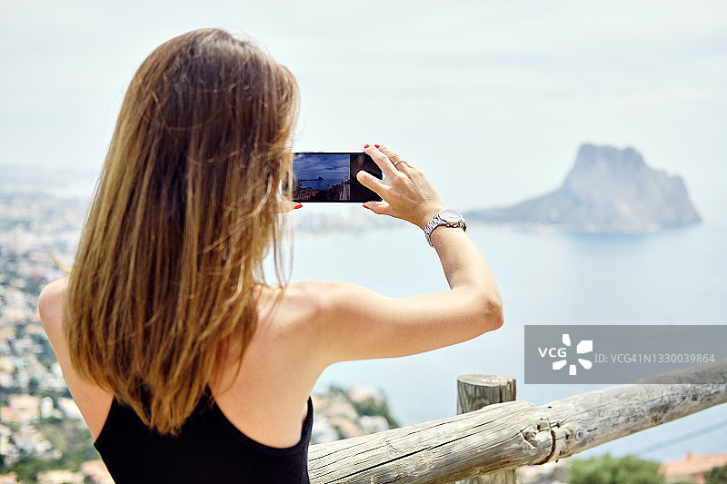 年轻女子用手机拍摄西班牙卡尔佩的自然美景图片素材
