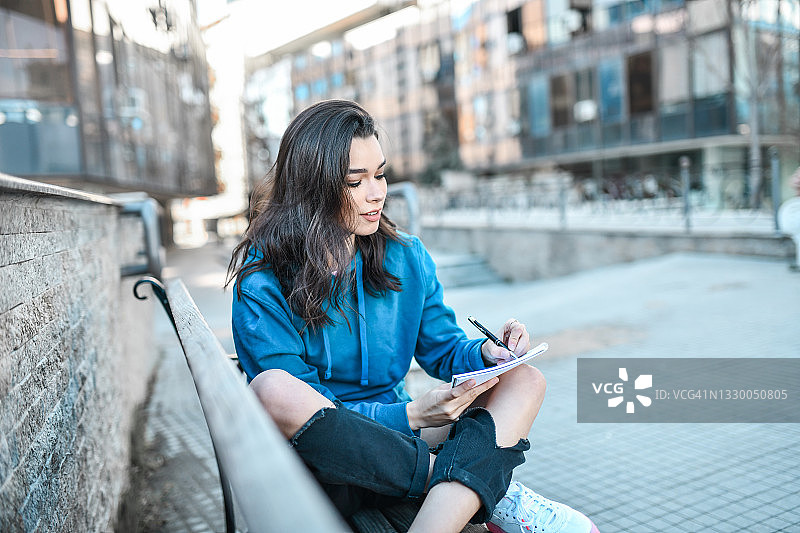 女学生坐在外面长椅上为学校写诗图片素材
