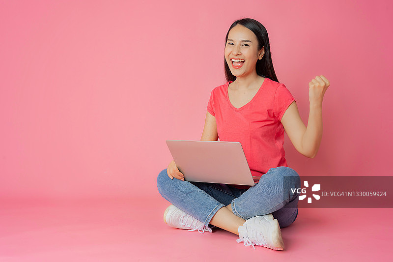 穿着红色衣服和休闲牛仔裤的亚裔女人坐在地板上使用笔记本电脑图片素材
