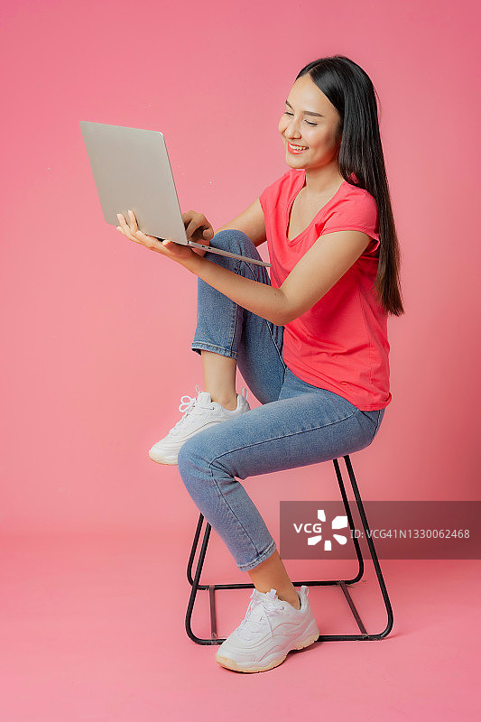 穿着红色衣服和休闲牛仔裤的亚裔女人坐在地板上使用笔记本电脑图片素材