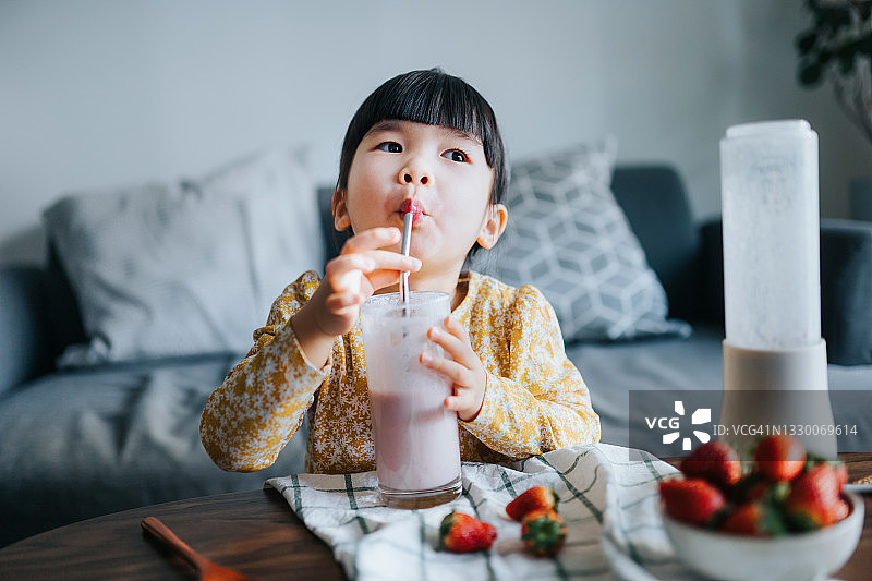 可爱的小亚裔女孩在家喝自制草莓冰沙，享受健康生活图片素材