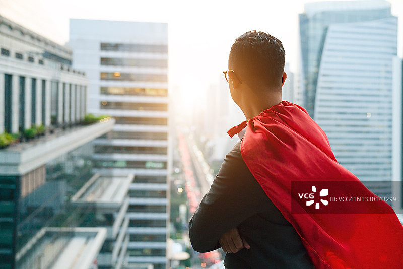 日落时分眺望城市天际线的超级英雄商人：商业成功、领导力和胜利图片素材