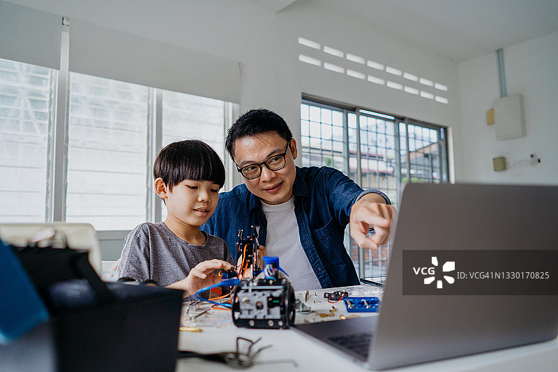 亚裔男孩和父亲在家一起组装机器人玩具图片素材