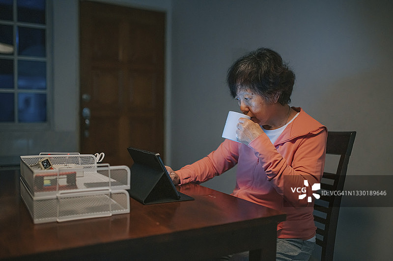 华人老年妇女在厨房使用平板电脑上网喝咖啡图片素材