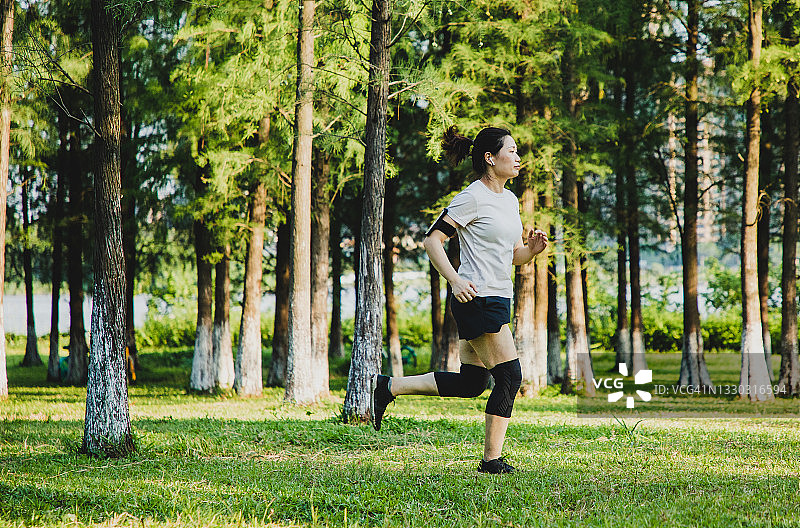 在公园慢跑的亚洲女人，戴着无线入耳式耳机，手臂上戴着智能手机图片素材
