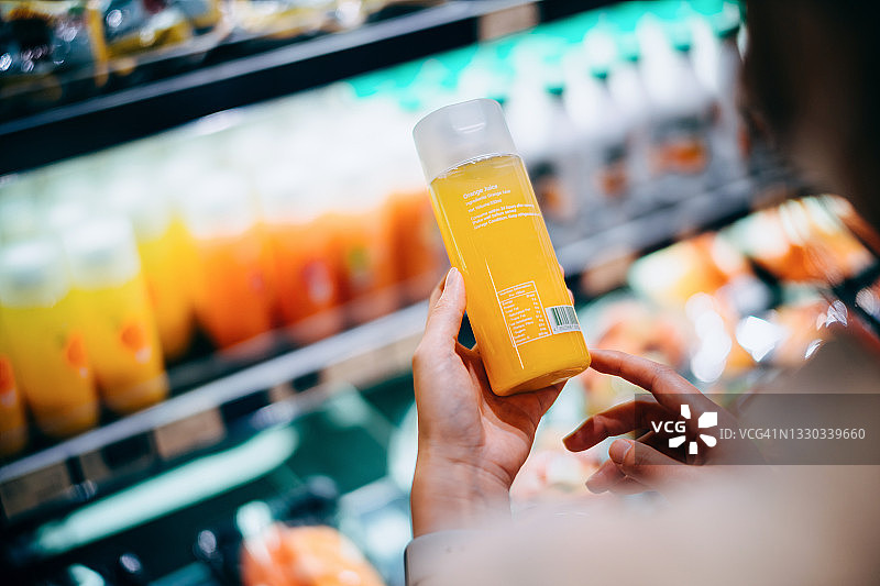 年轻亚洲女性在超市购物，正在阅读橙汁瓶上的营养标签图片素材