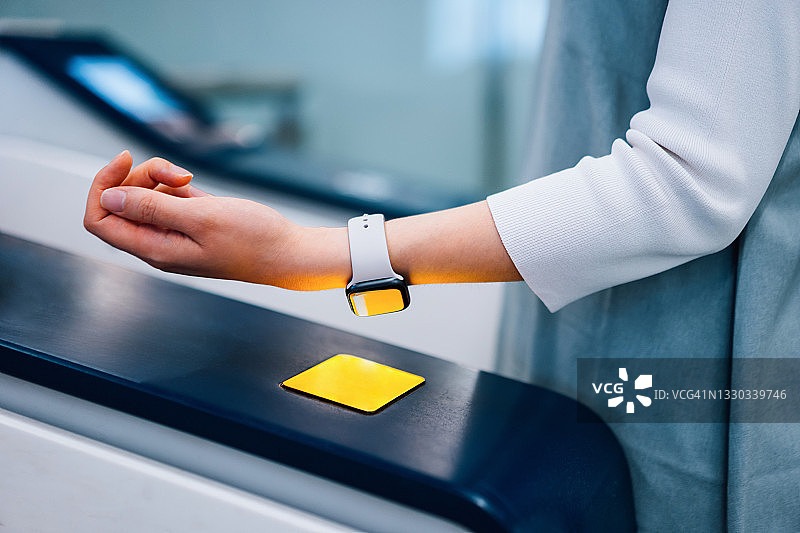 年轻亚洲女子在地铁站办理登机手续，通过智能手表快速便捷地进行非接触式地铁票支付，NFC技术，即触即走概念图片素材