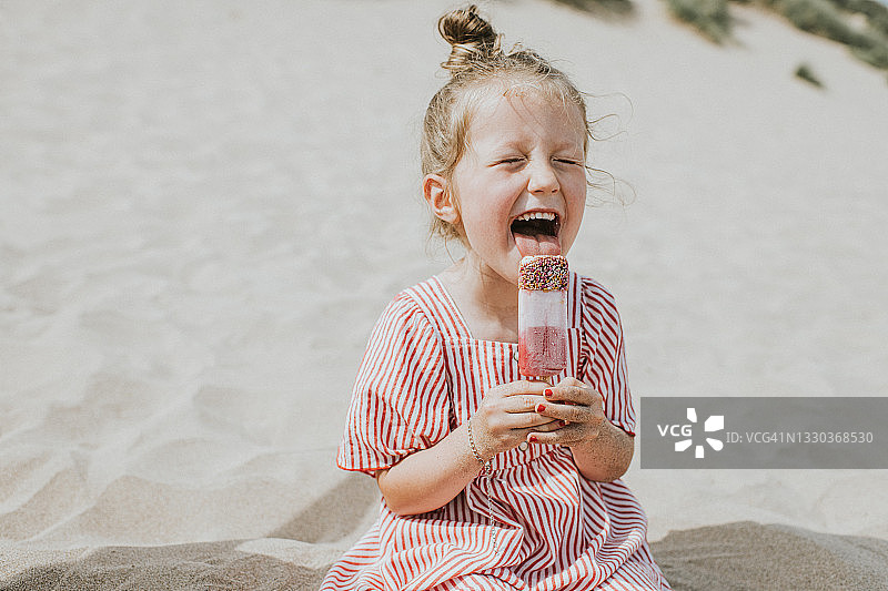 可爱女孩坐在海滩上舔冰棒图片素材