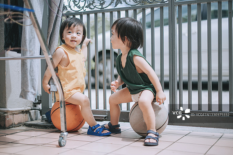 中国双胞胎男婴在夏季周末坐在房子前的篮球上图片素材