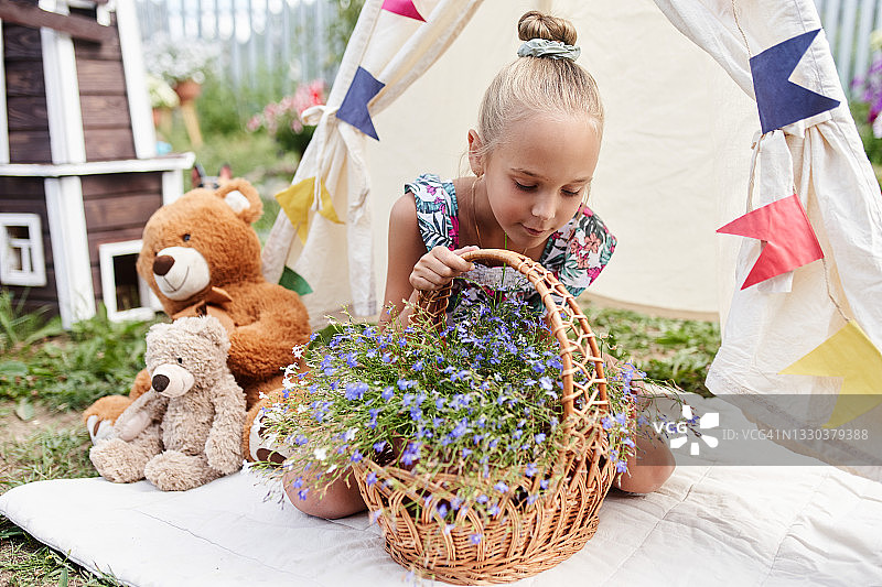 女孩坐在后院儿童帐篷里欣赏一篮鲜花图片素材