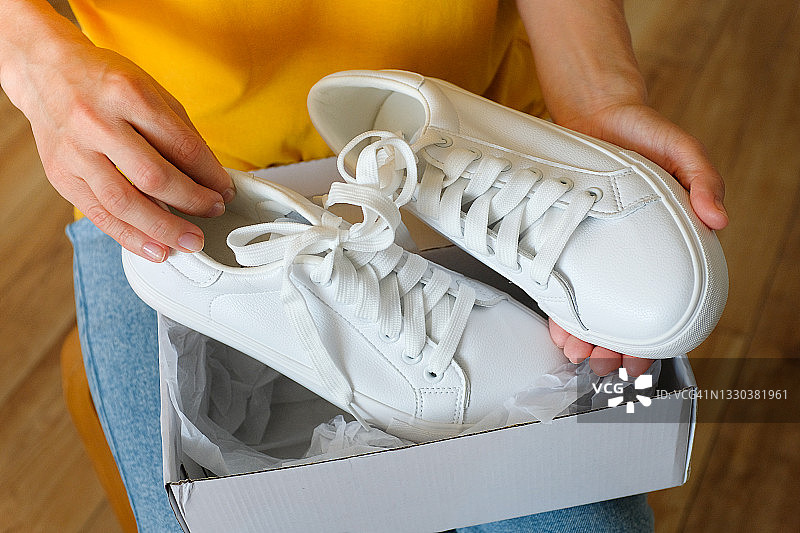 女孩从包装中取出新的干净的白色现代运动鞋，女人或青少年在家中或室内从盒子中打开运动鞋，在家订购和交付衣服和物品，居家，时尚的生活方式图片素材