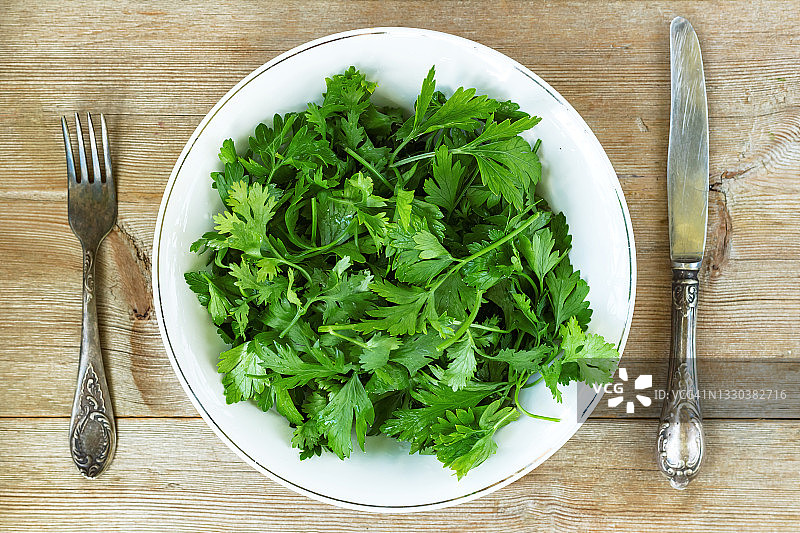 旧木桌背景上的绿色香草沙拉、叉子、刀子拼盘，排毒概念图片素材