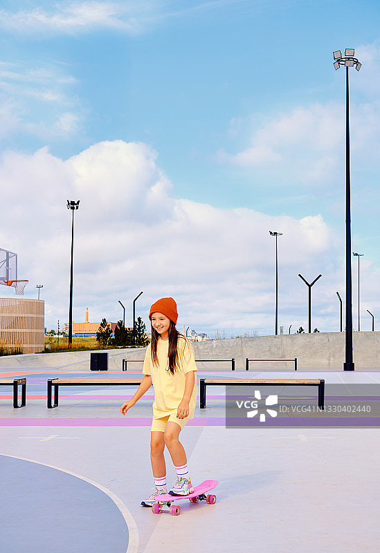 戴着红帽子的女孩在白云背景下滑滑板。一个年轻女孩在做运动。图片素材