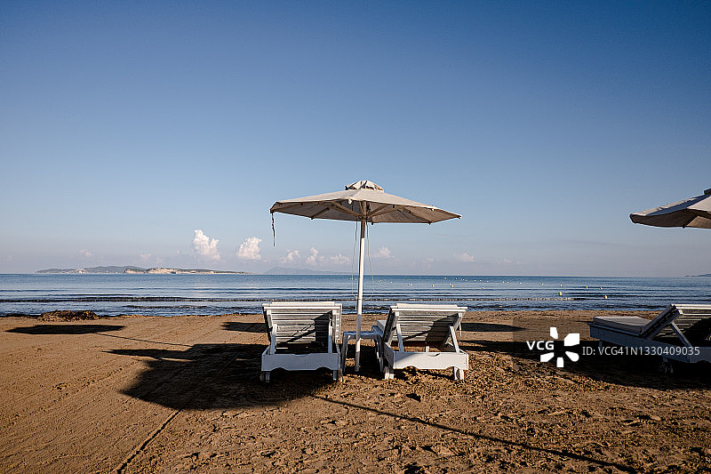 海滩上带遮阳伞的白色日光浴床面向大海图片素材